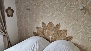 Une chambre avec deux lits, une tête de lit ornée d’un motif de feuilles et un luminaire fixé au mur.