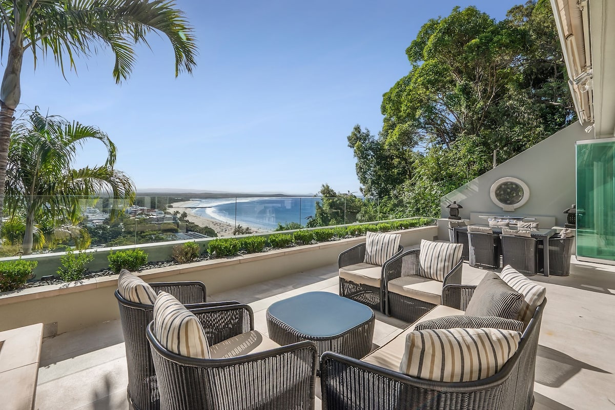 Un balcon agrémenté de meubles en osier, d’une table ronde et offrant une vue sur la plage et l’océan.