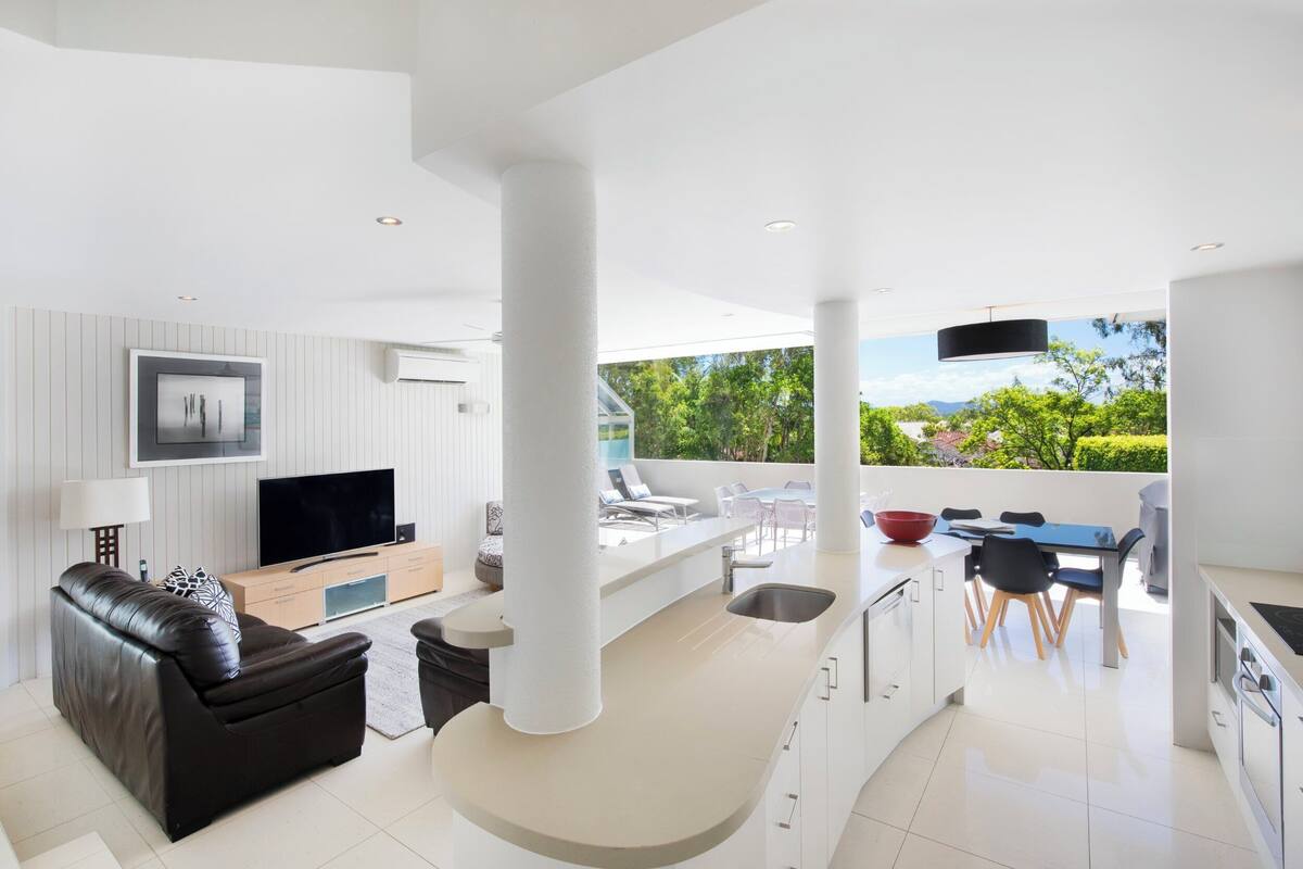 Un salon moderne avec un canapé, un téléviseur et un coin repas, ainsi qu’un espace détente extérieur.