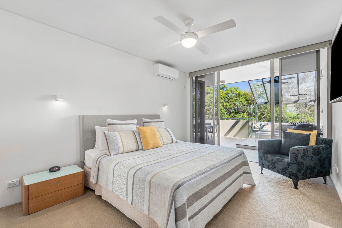 A bedroom with a bed, a nightstand, a chair, a ceiling fan, and a sliding glass door leading to an outdoor area.