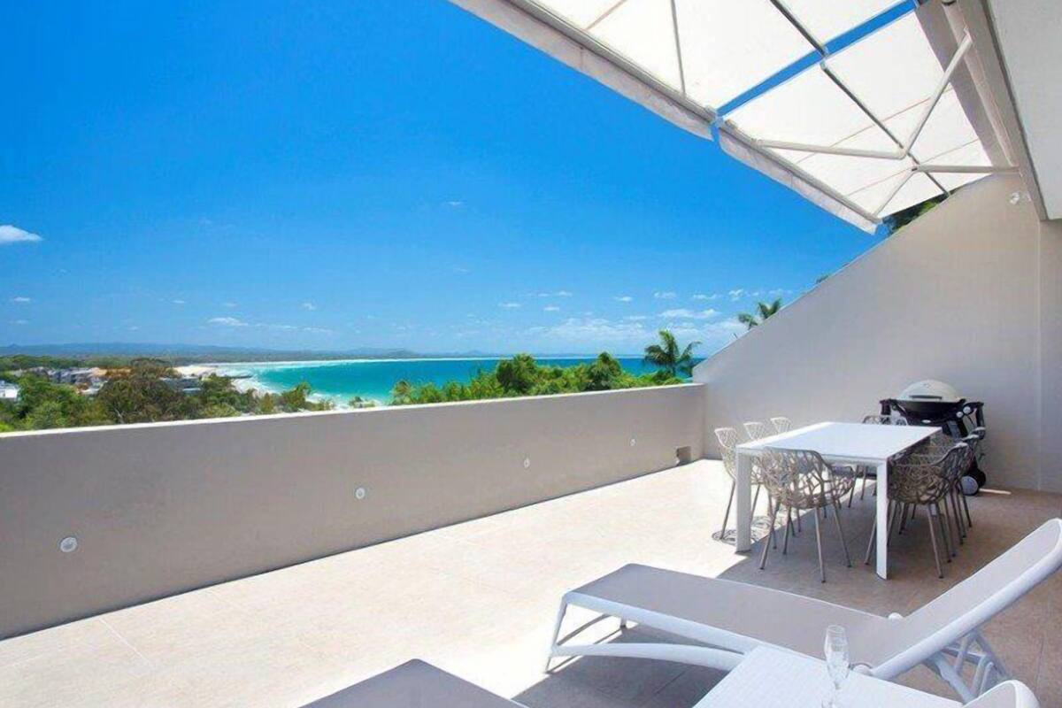 Un balcon avec une table et des chaises, donnant sur une plage et l’océan.