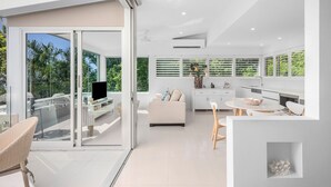 Ein modernes Interieur mit einer Glastür zum Balkon, ein weißes Sofa, ein Esstisch mit Stühlen und eine Küchenzeile mit weißen Schränken und einem eingebauten Backofen.