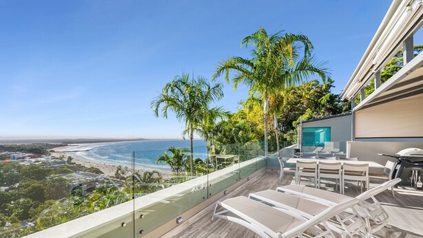 Ein Balkon mit Blick auf Strand und Meer, mit Gartenmöbeln und Glasgeländer.