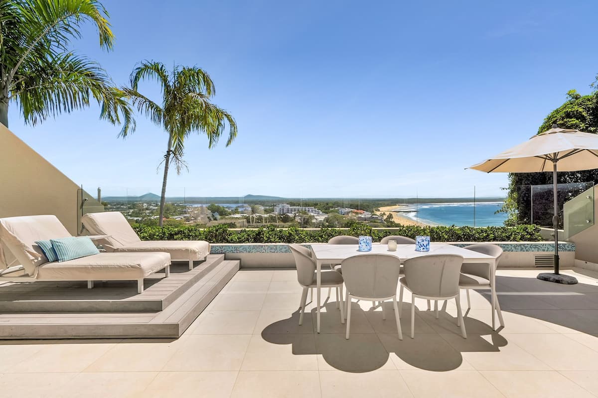 Une terrasse extérieure avec une table et des chaises, un transat et une vue sur la plage.