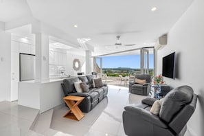 A modern living room with a sofa, armchair, and a dining area with a white table. - Number One In Hastings Street (Noosa Heads)