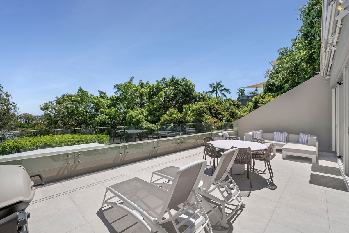 A rooftop patio with outdoor seating, a grill, and a view of greenery and buildings.