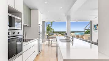 A modern kitchen with a view of the ocean, a dining area with a table and chairs, and a large window.