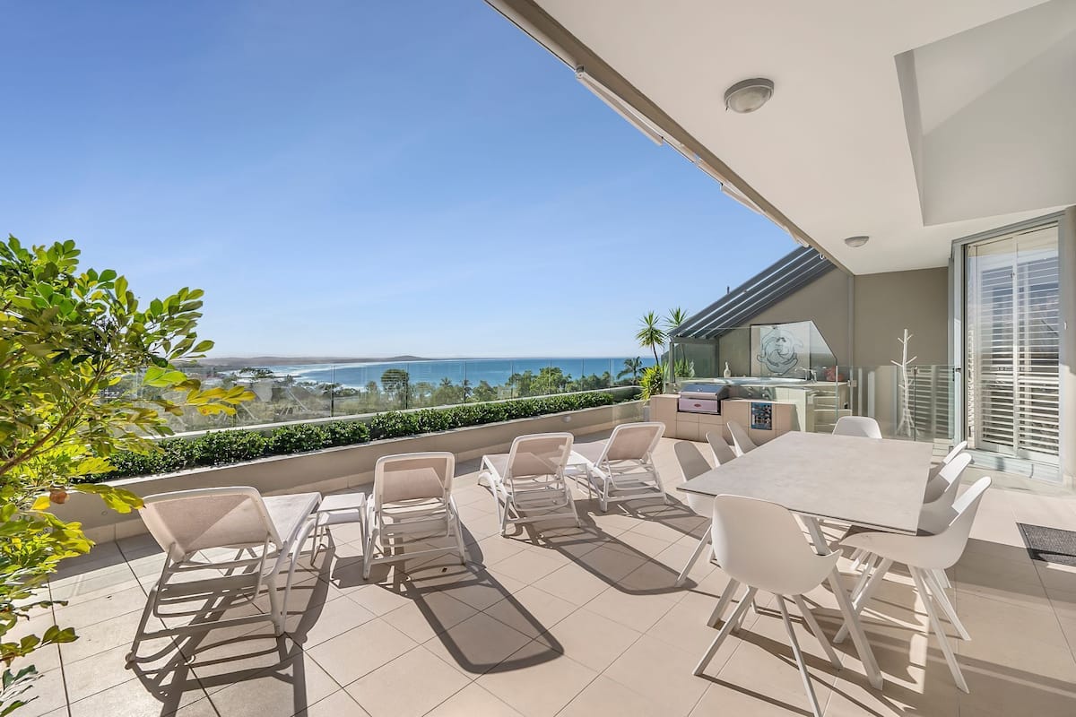 Une terrasse avec une table et des chaises, une balustrade en verre et une vue sur la mer.