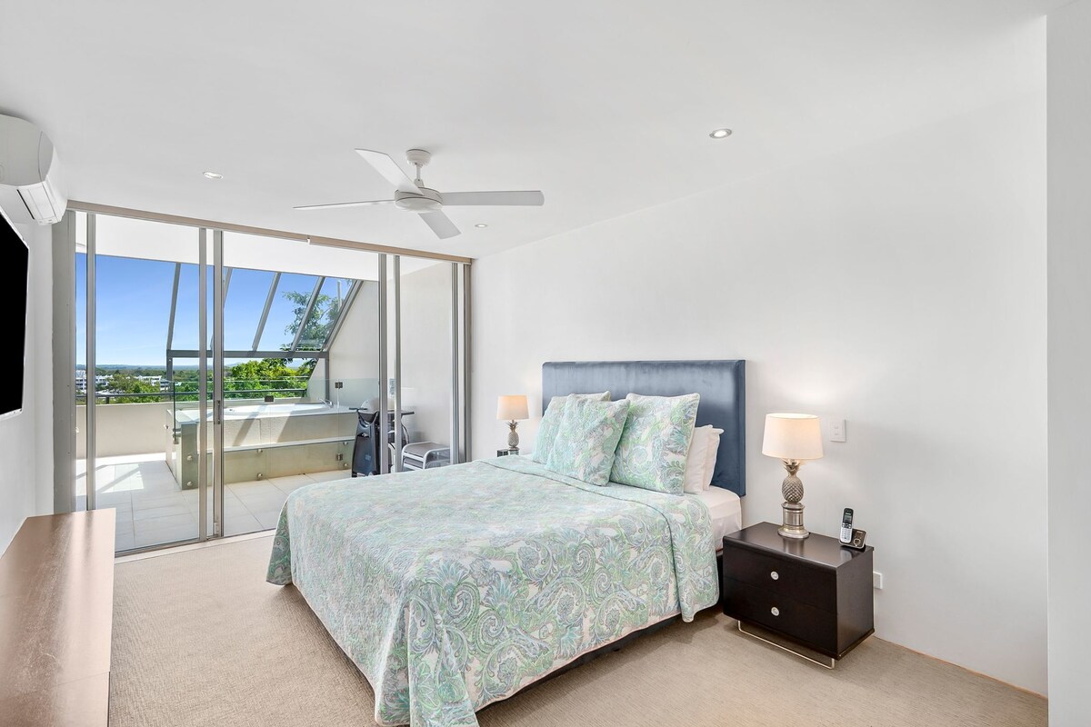 A bedroom with a bed, nightstands, a ceiling fan, and a view through a sliding glass door.