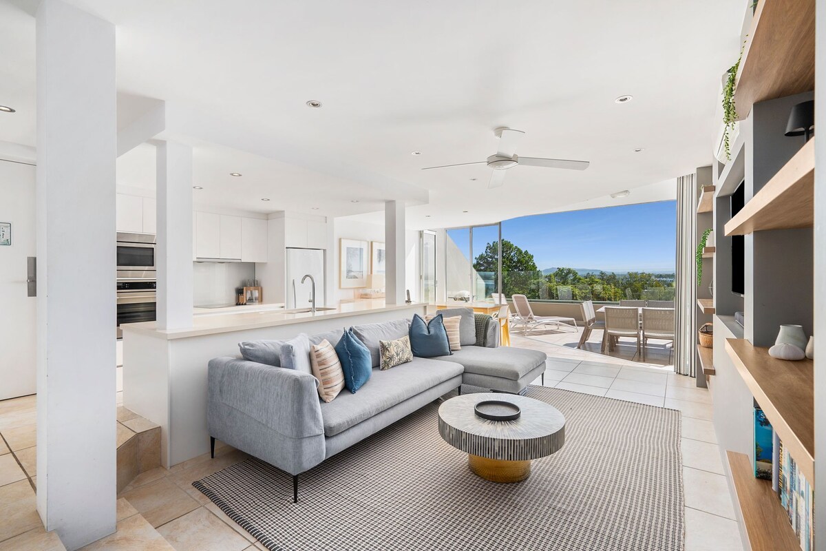 A modern living room with a grey sectional sofa, a round coffee table, and a view of the outdoors.