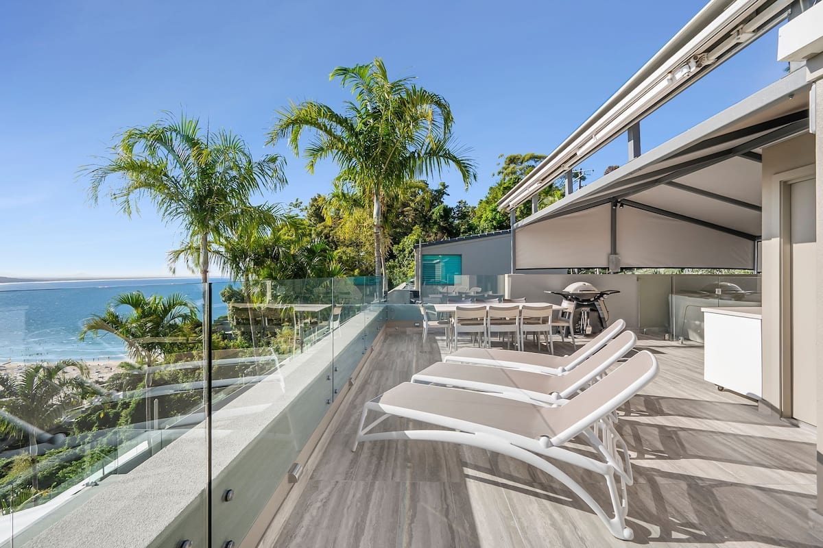 Un balcon avec des fauteuils de jardin, une balustrade en verre et une vue sur l’océan.