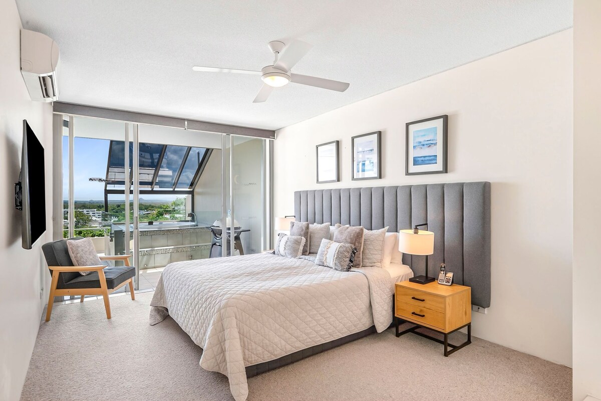 A bedroom with a bed, bedside table, chair, and a view through a glass door.
