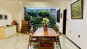 Un coin repas avec une table et des chaises en bois, un comptoir de cuisine et un escalier menant à un balcon agrémenté de plantes.