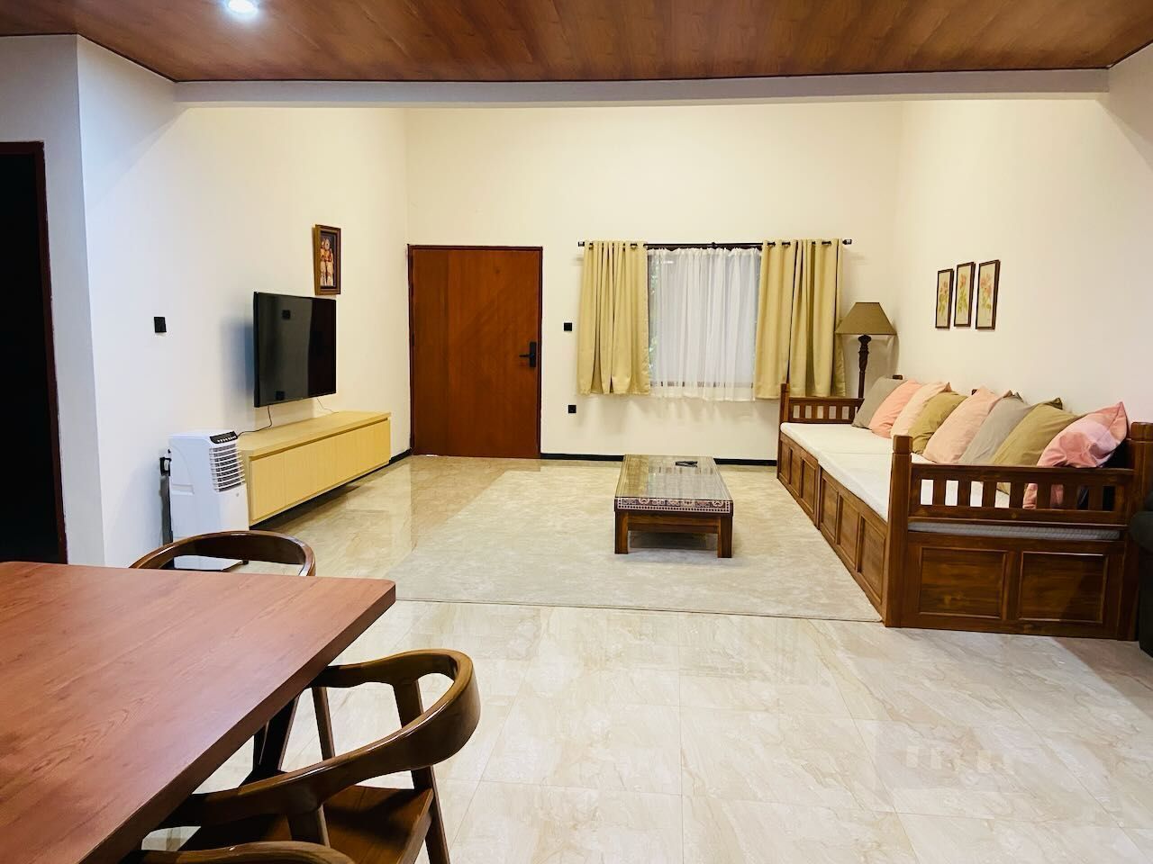 A living room with a wooden dining table, a sofa, a TV, and a window with curtains.