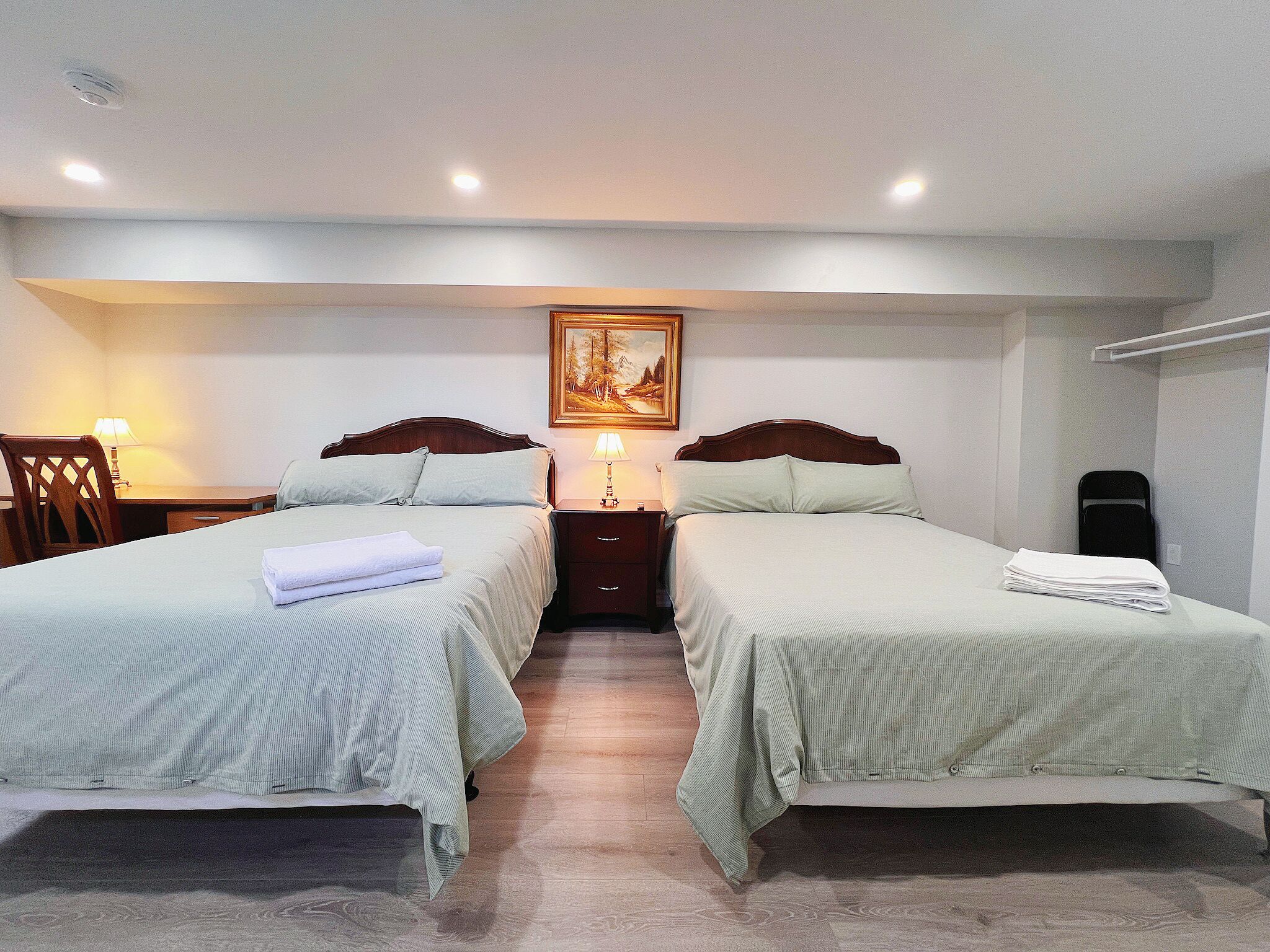 A hotel room with two beds, a desk, a chair, a lamp, and a painting on the wall.
