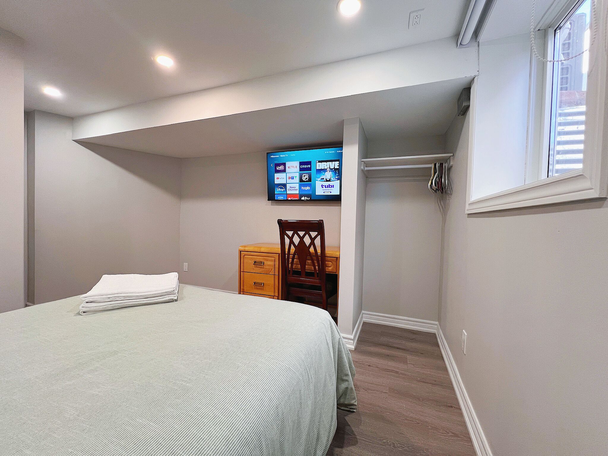 A bedroom with a bed, a dresser, a TV mounted on the wall, and a window.