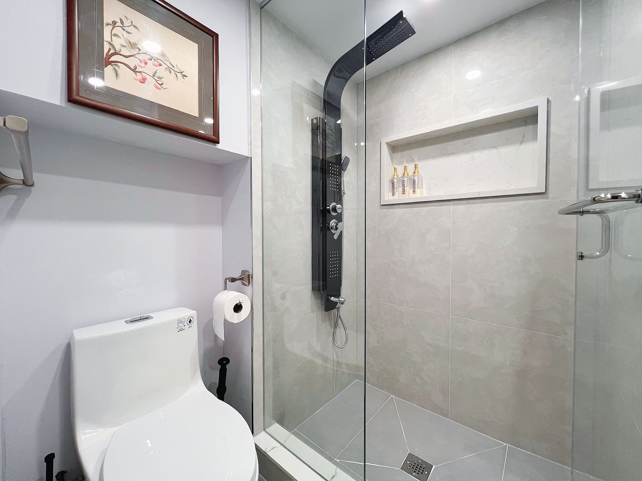 A bathroom with a toilet, a glass-enclosed shower, and a shelf with toiletries.