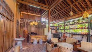 A traditional wooden interior with a central seating area, patterned floor, and shelves with pottery. - JavaLO Lite (Pujut)