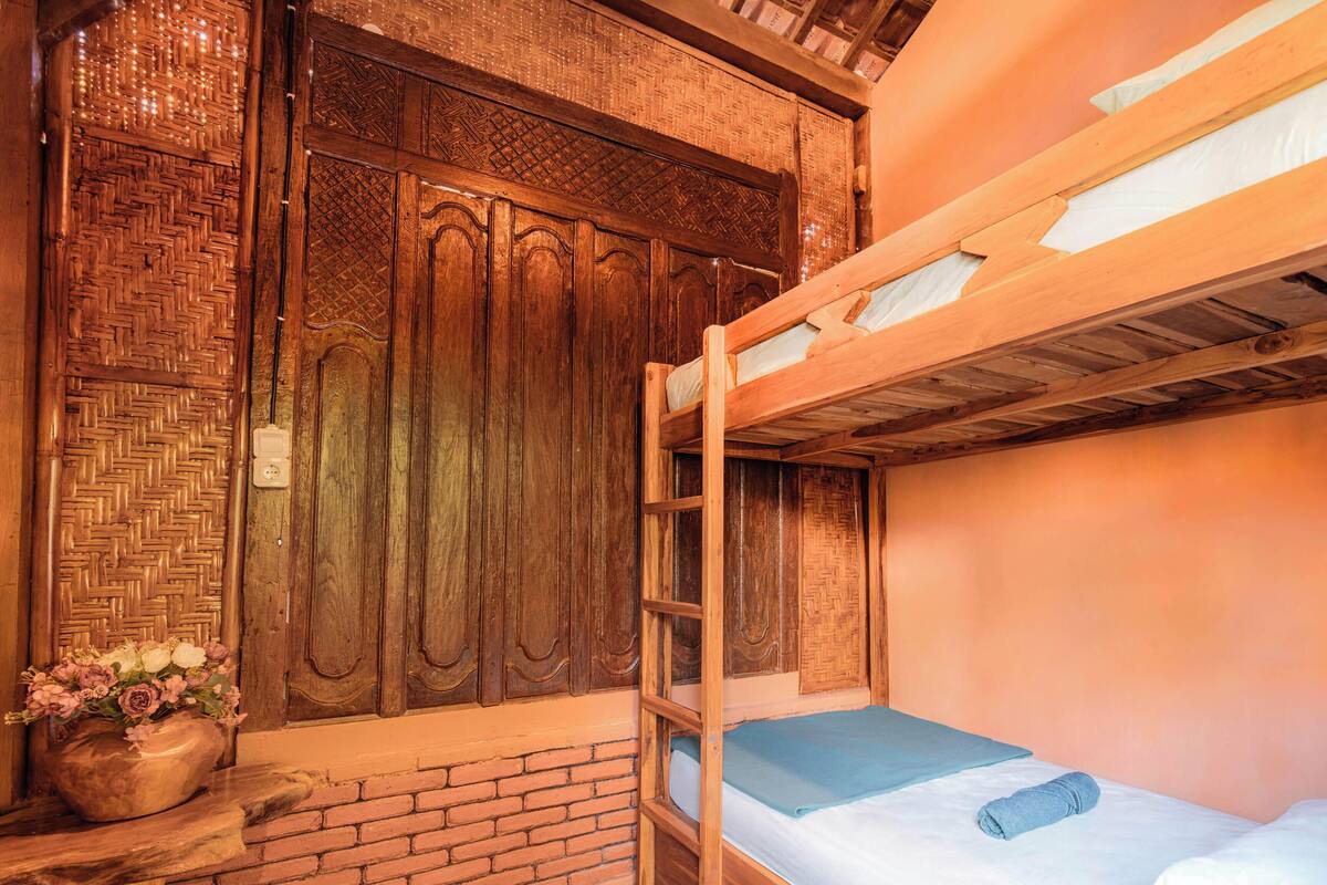 A wooden bunk bed with a blue mattress, a wooden door with intricate carvings, and a brick wall.