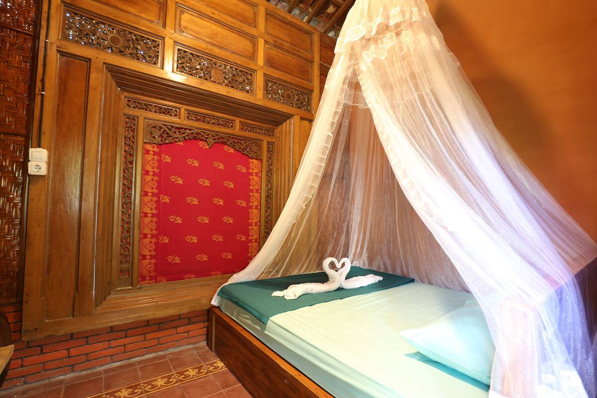 A room with a bed under a canopy, a red patterned door, and a brick wall.