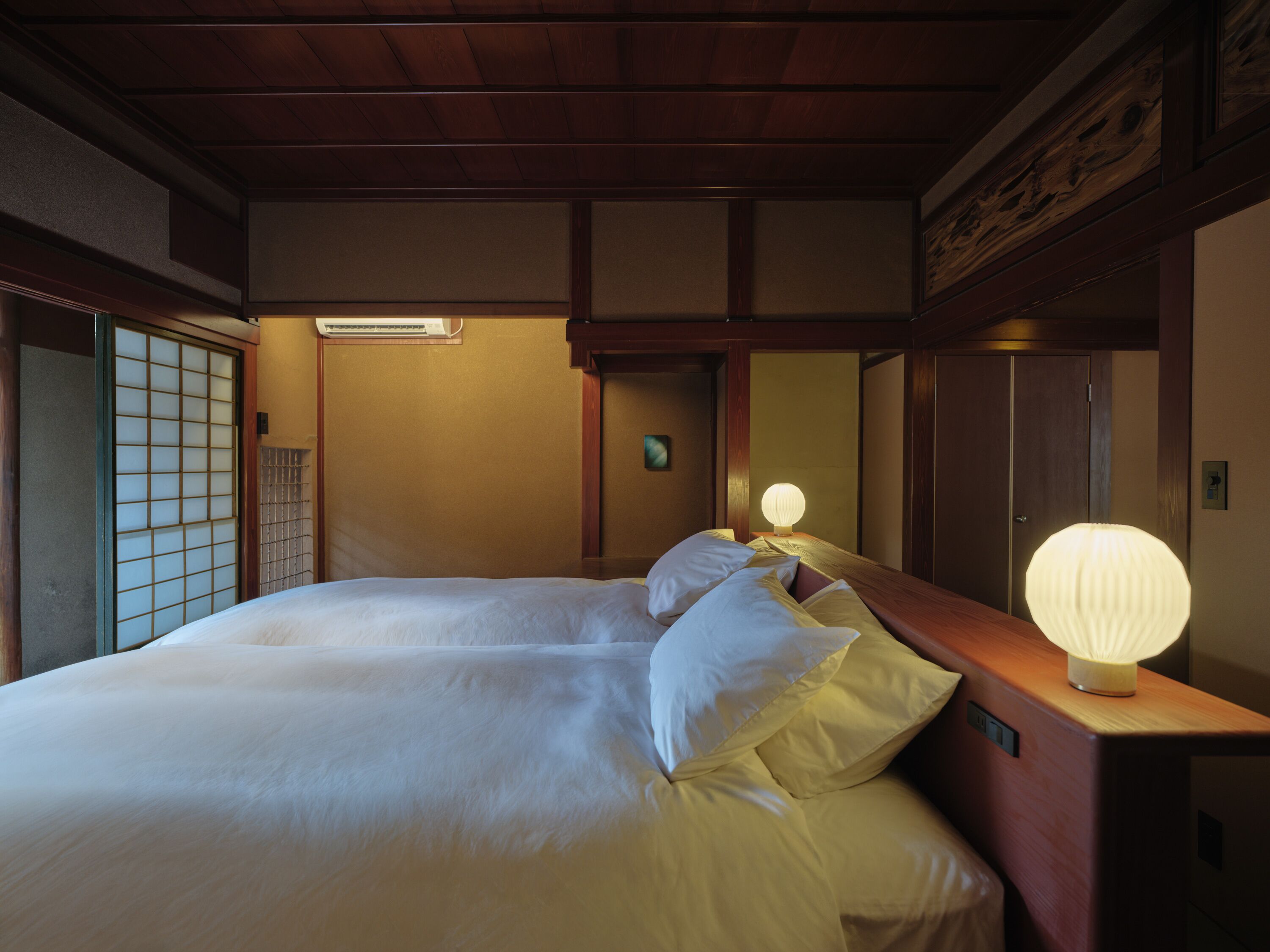 Una habitación de estilo japonés tradicional con suelo de tatami, una cama baja de madera con ropa de cama blanca y una puerta corredera shoji.