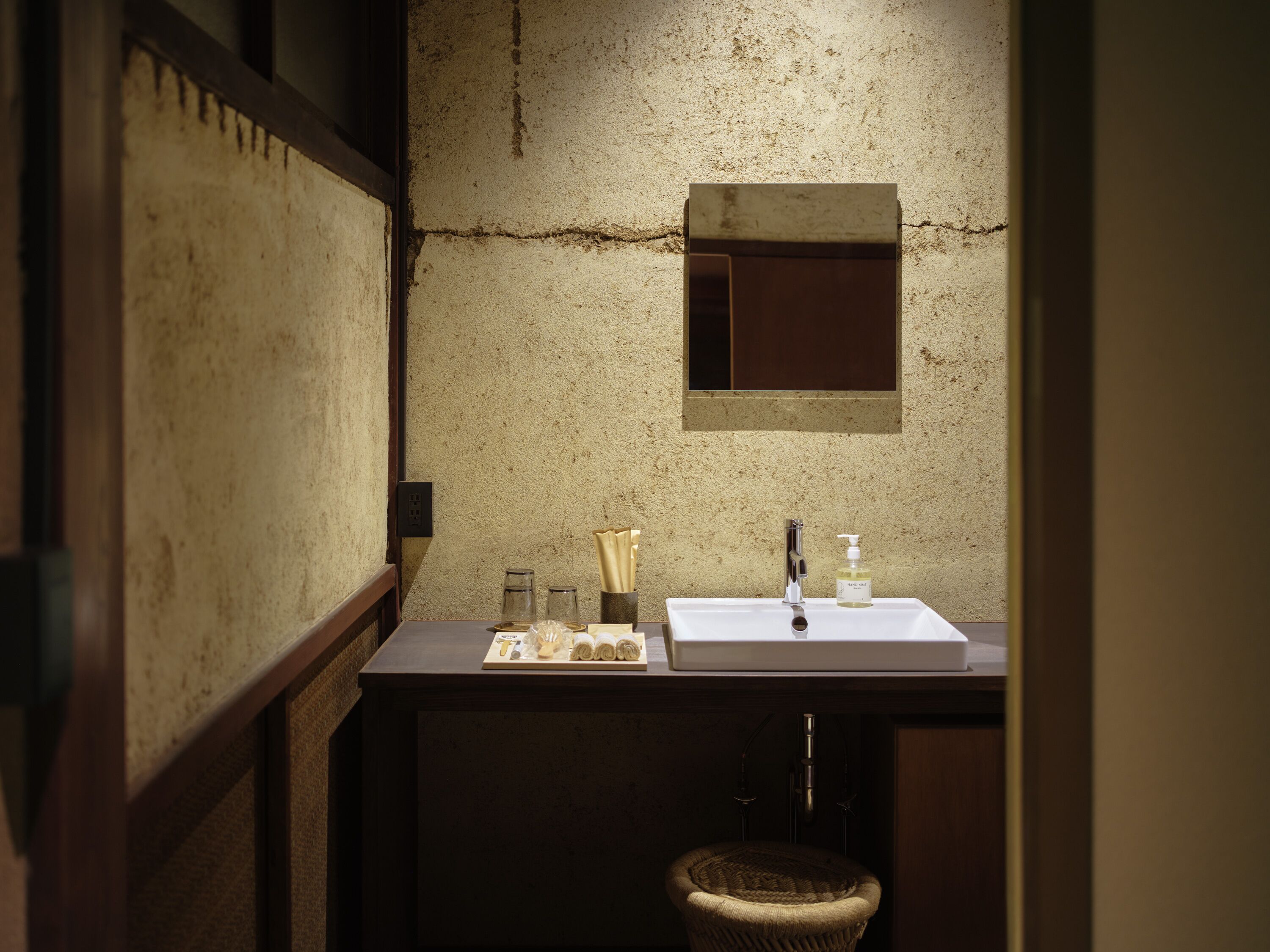 A compact bathroom with a white sink, a small mirror, and a wooden stool.