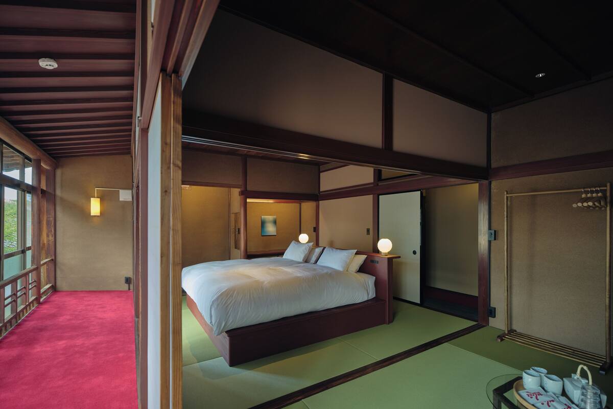 A traditional Japanese-style bedroom with tatami flooring, a large bed with white bedding, and a small table with tea set.