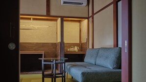 A traditional Japanese room with tatami flooring, a low table, a sofa, and a wooden partition. - Komado Bengara (Komatsu)