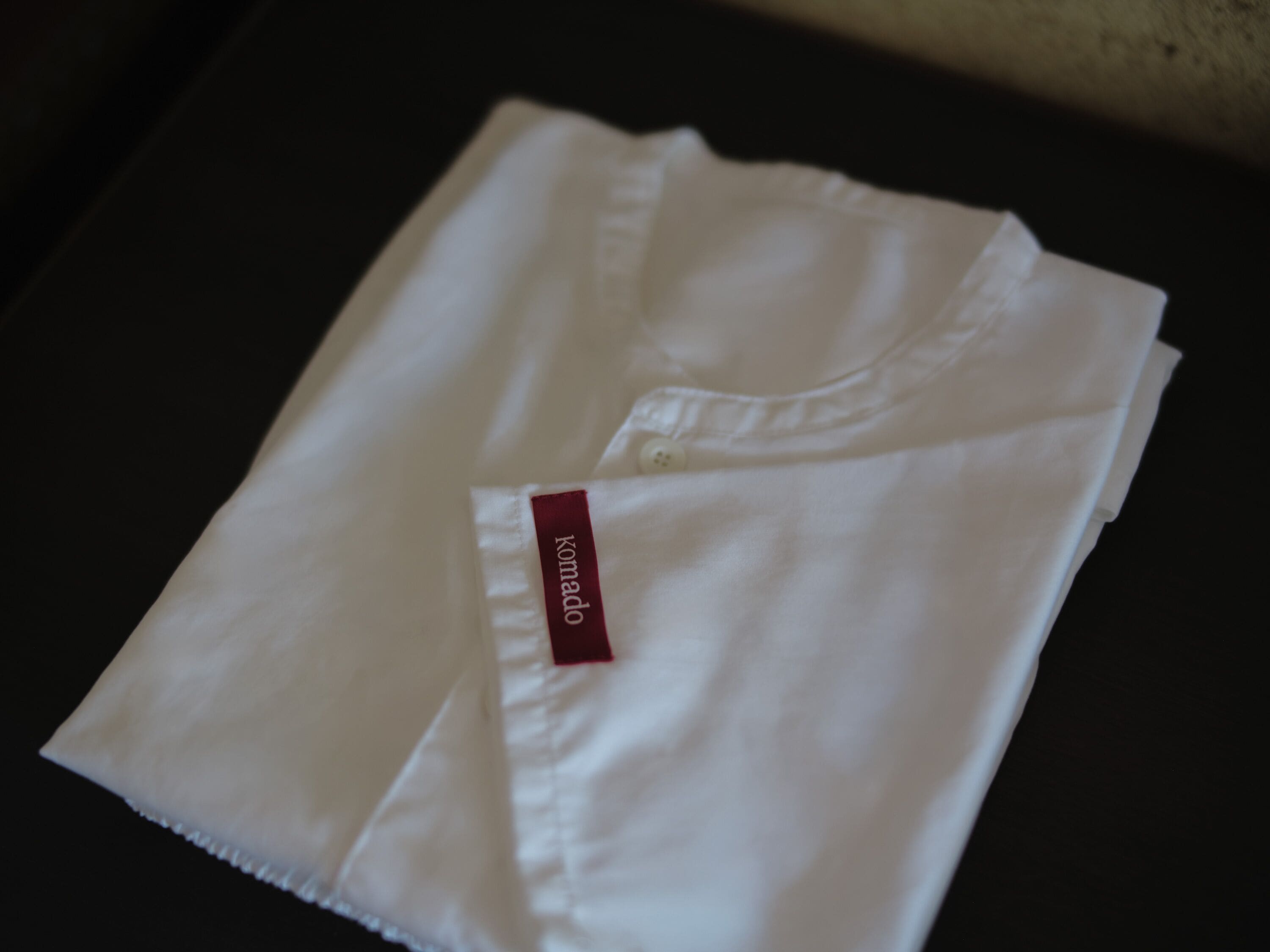 Camisa branca dobrada com etiqueta vermelha sobre uma superfície escura.