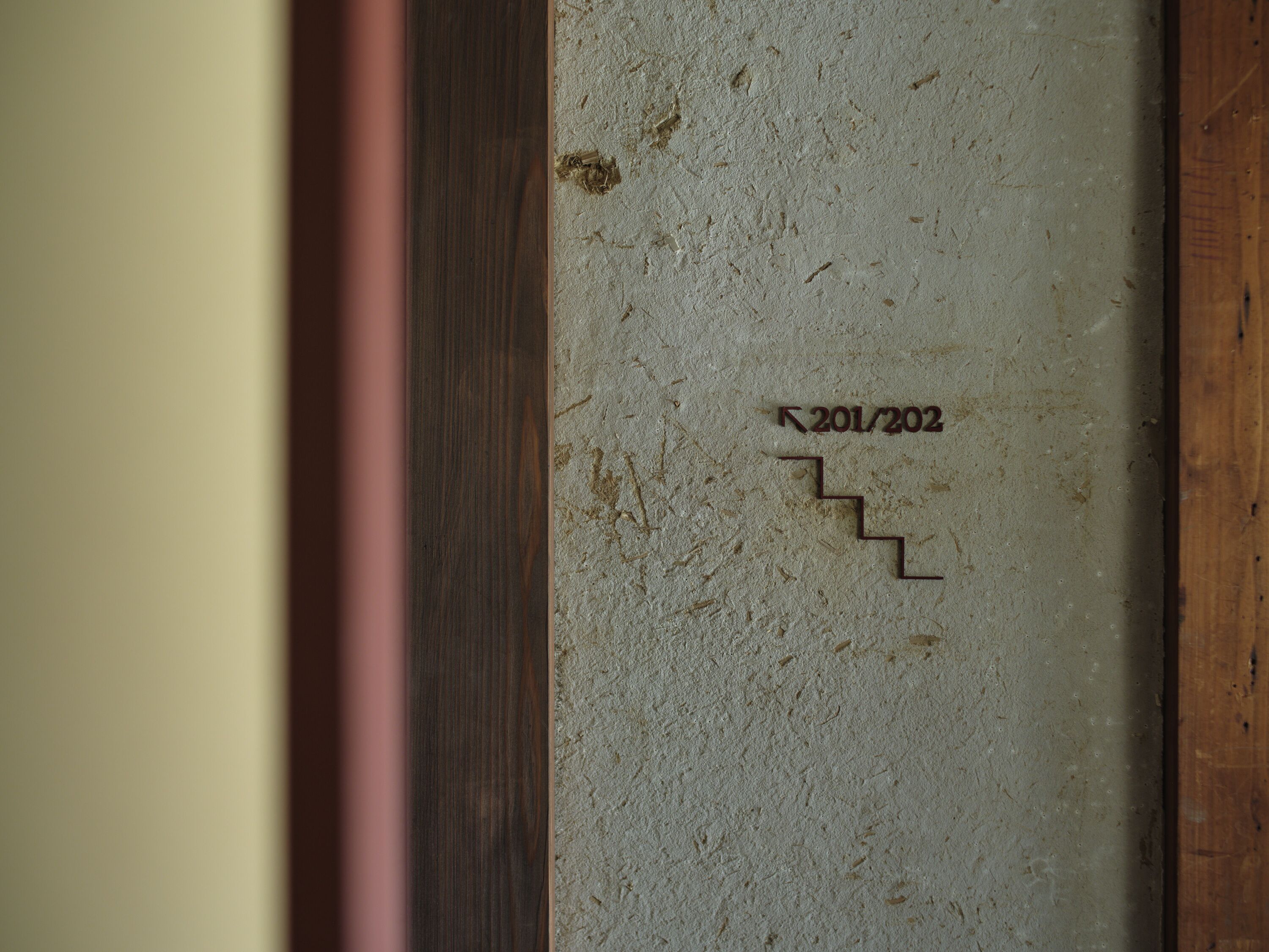 A textured wall with a wooden frame and a small, dark inscription reading "201/202".