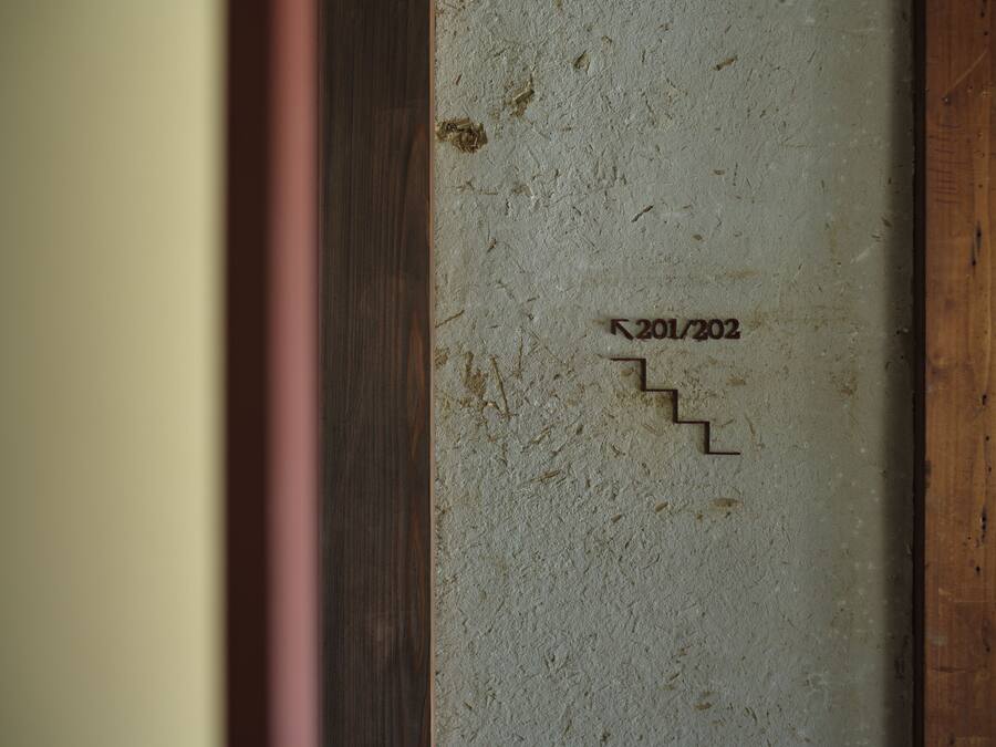 A textured wall with a wooden frame and a small, dark inscription reading "201/202".