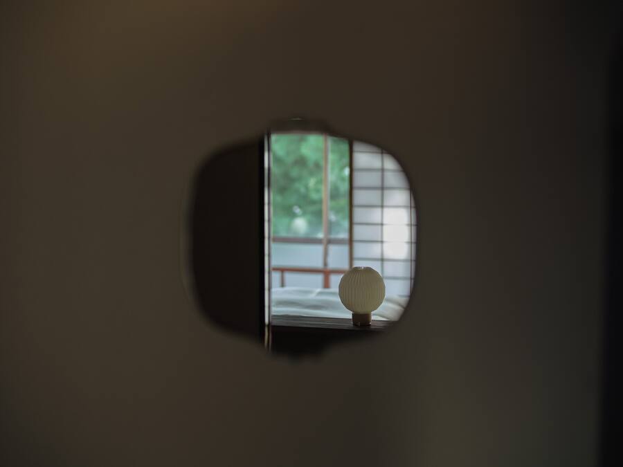A mirror reflecting a room with a bed and a window with a view of trees.