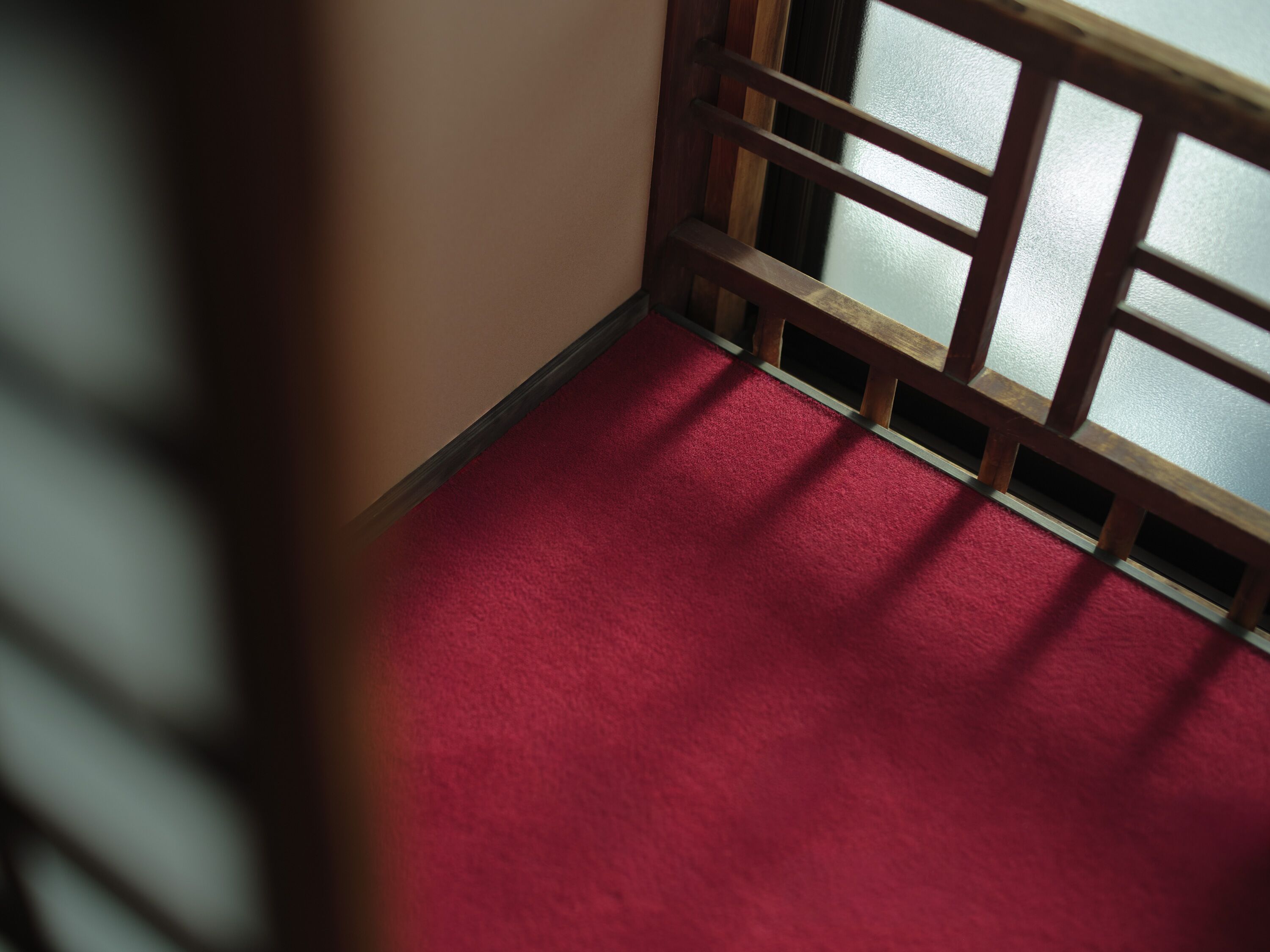 Esquina de una habitación con alfombra roja y un separador de madera con paneles de vidrio.