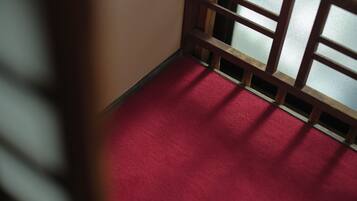 Esquina de una habitación con alfombra roja y un separador de madera con paneles de vidrio.