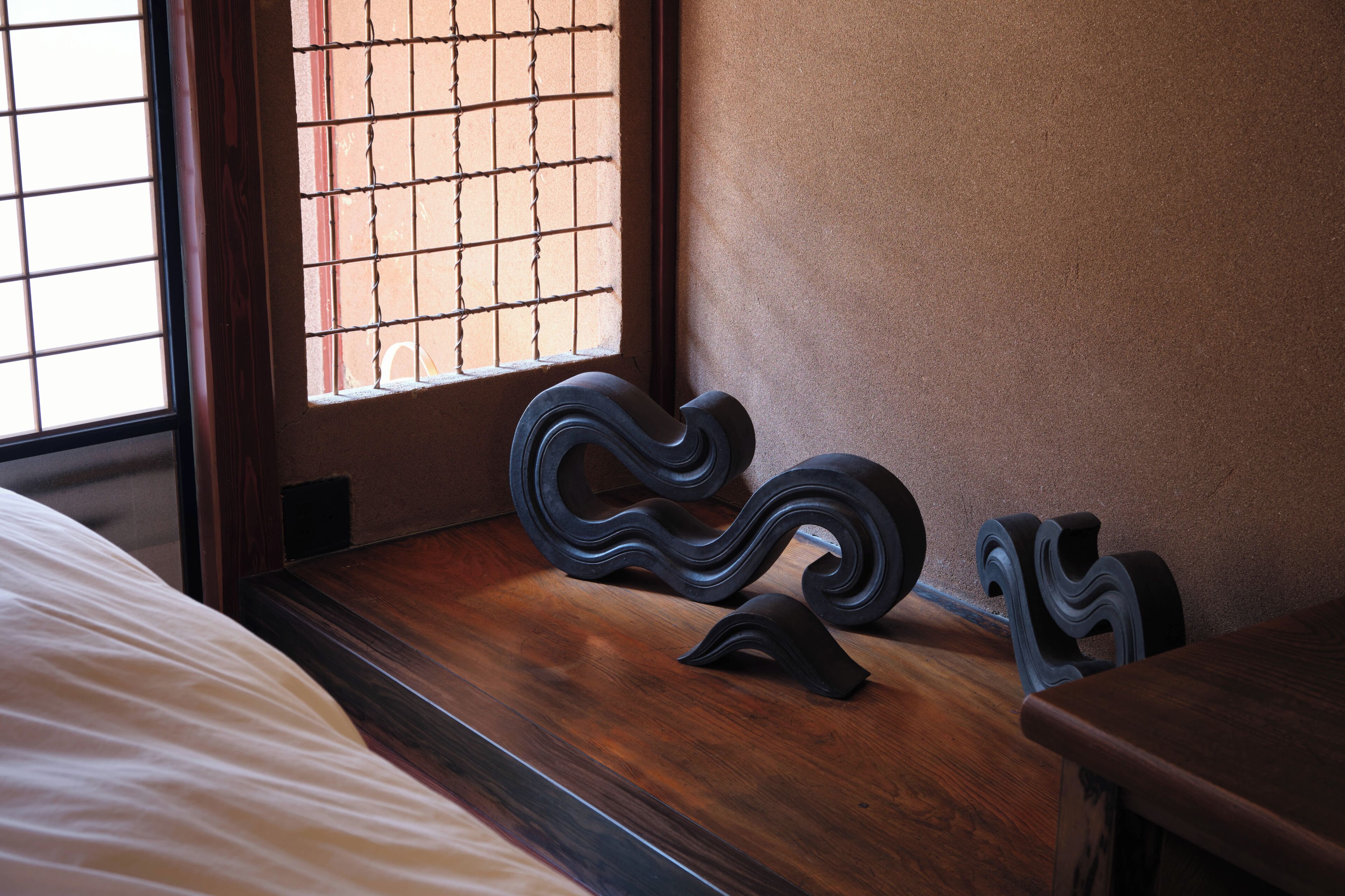A wooden bedside table with a curved design, a window with a grid pattern, and a bed with white bedding.