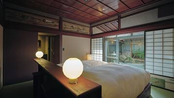 A traditional Japanese-style bedroom with a large bed, sliding doors, and a view of a garden.