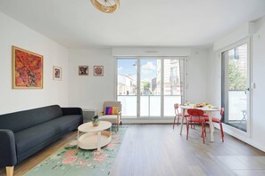 Un soggiorno moderno con un divano, un tavolino, un tavolo da pranzo con sedie e un'ampia porta scorrevole in vetro che si apre su un balcone esterno.