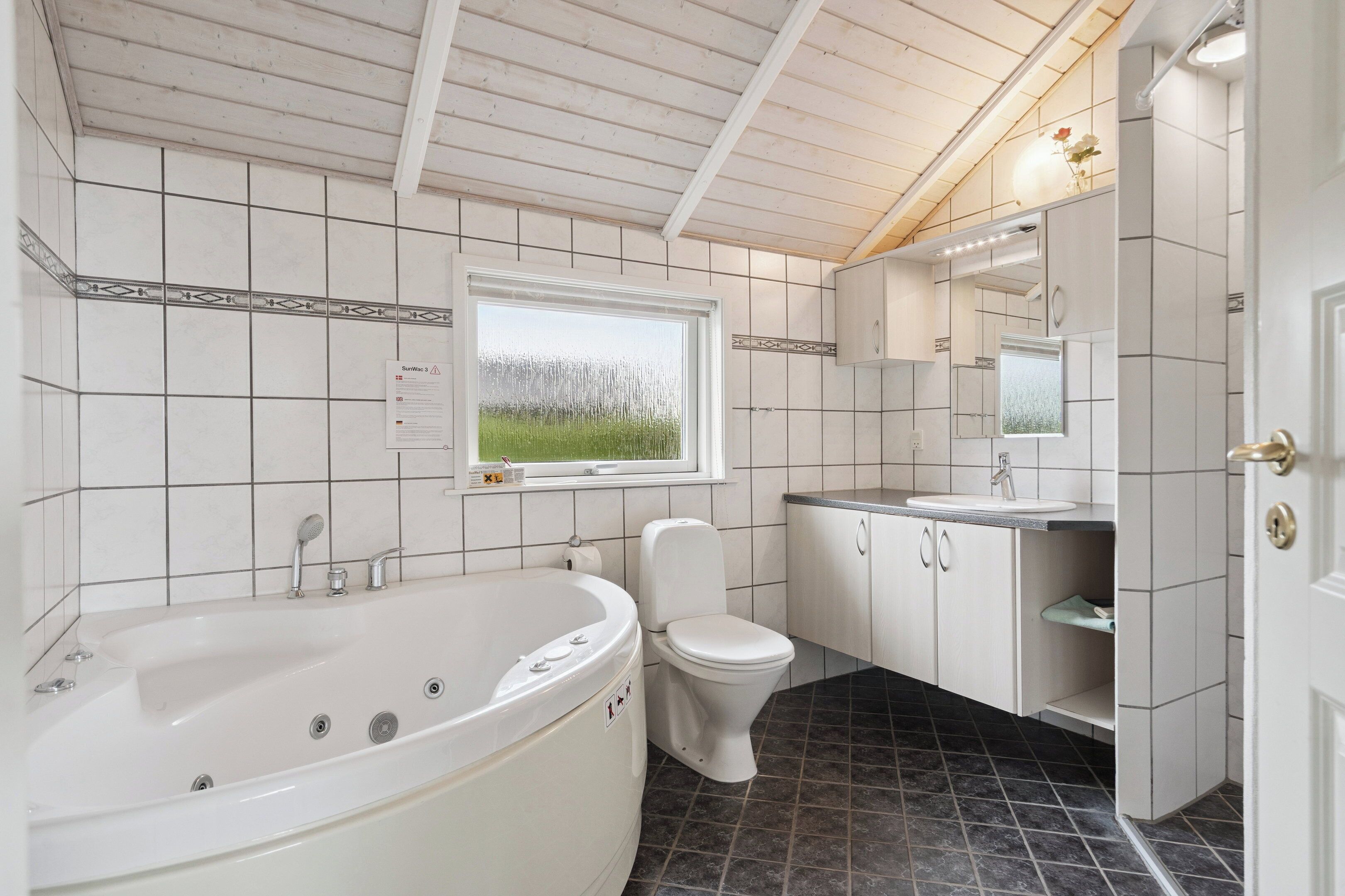A bathroom with a bathtub, toilet, sink, and a window with a view of a field.