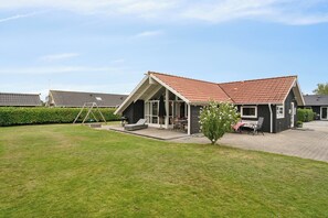 Een woongebouw met een schuin dak, een terras met tuinmeubilair en een verzorgd gazon.