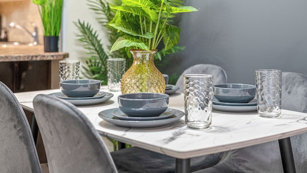 A dining table set with plates, bowls, and glasses, surrounded by chairs.