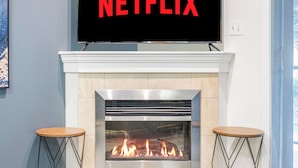 A modern living room with a fireplace, a television mounted above it, and two wooden stools.