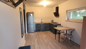 A compact kitchen with a refrigerator, sink, and a small dining table with chairs. - Tauralaukis forest & terrace, free parking (Klaipėda)