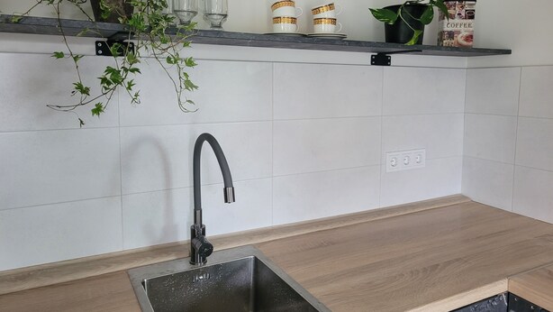 A kitchen with a stainless steel sink, a black faucet, a wooden countertop, and a shelf with plants and kitchenware. - Tauralaukis forest & terrace, free parking (Klaipėda)