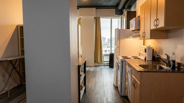 Een moderne keuken met houten kastjes, een inbouwoven en een raam met gordijnen.
