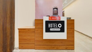 A reception desk with a sign that reads 'HOTELO Company-Serviced' and a clock above it. - Hotel O Pari Chowk Metro Station (Greater Noida)