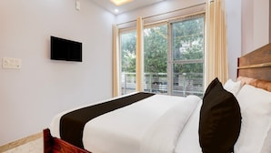 A modern hotel room with a bed, a TV on the wall, and large windows with a view of trees and a balcony. - Hotel O Pari Chowk Metro Station (Greater Noida)