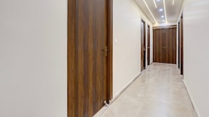 A corridor with wooden doors and a tiled floor. - Hotel O Pari Chowk Metro Station (Greater Noida)