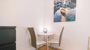 A corner room with a small round table and two chairs, a painting of a boat on a frozen lake, and a black cabinet. - Modern 2BR Apt Longstay Sleeps 5 (Vienna)