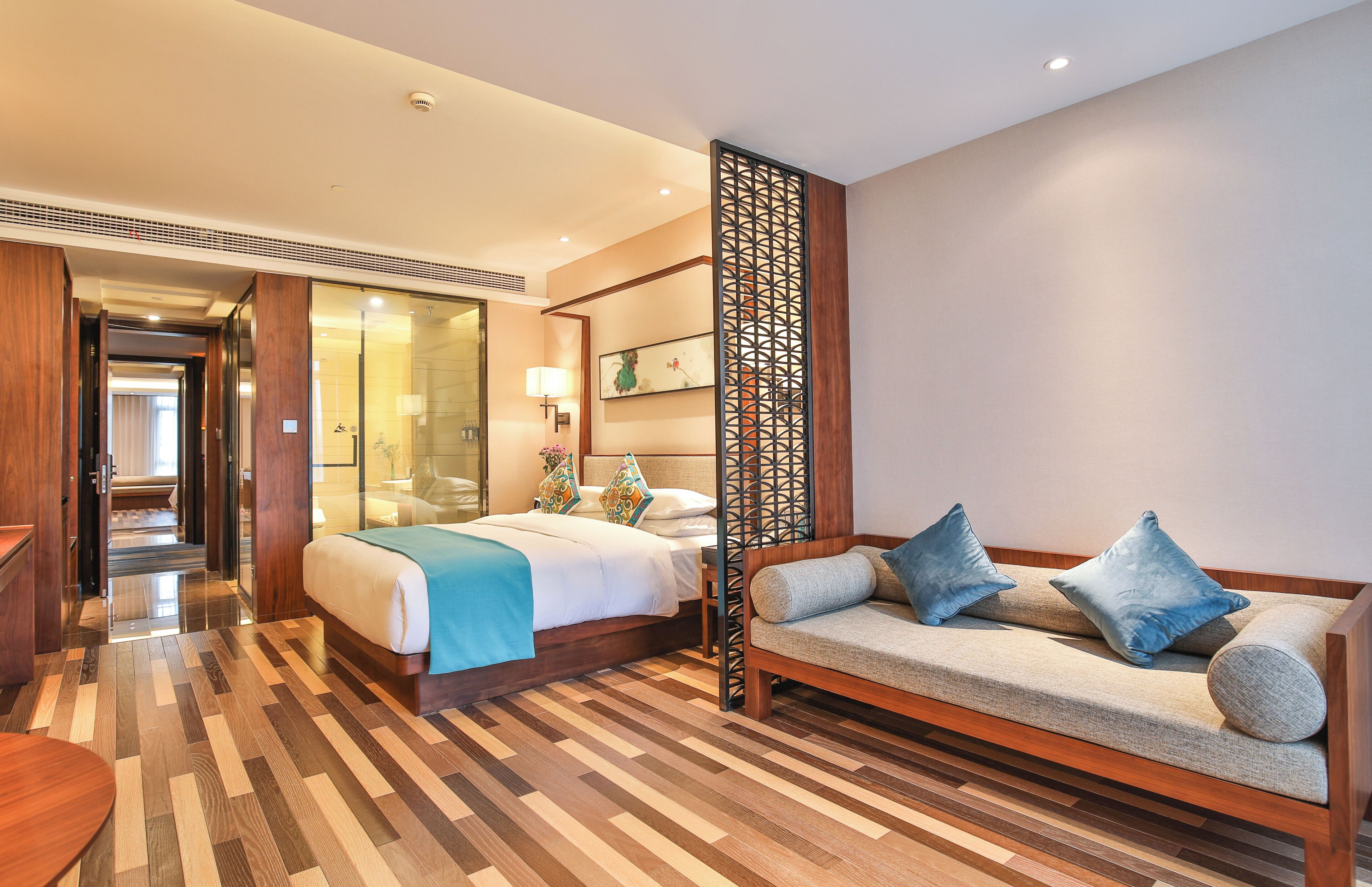 A hotel room with a bed, a sofa, a wooden floor, and a decorative screen.