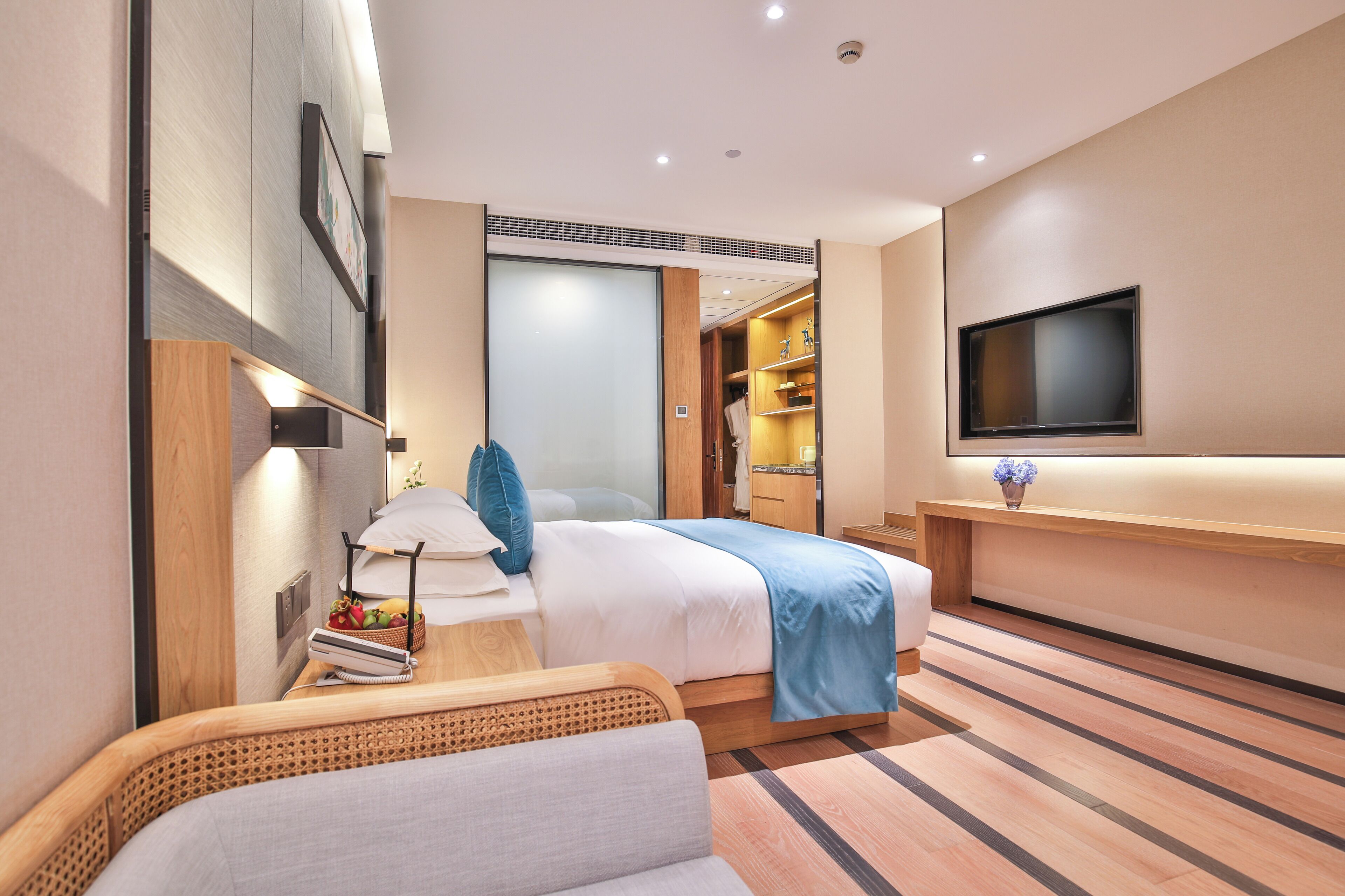 A modern hotel room with a bed, bedside table, lamp, and a TV mounted on the wall.